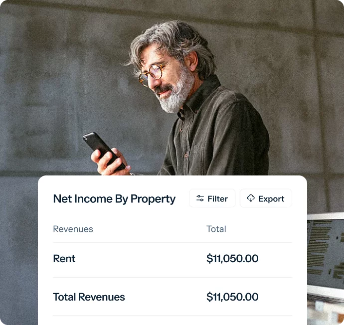 A man with gray hair and a beard wearing glasses is looking at his smartphone. In front of him is a table titled "Net Income By Property" showing revenues: Rent $11,050.00 and Total Revenues $11,050.00. Options to filter and export data are visible.