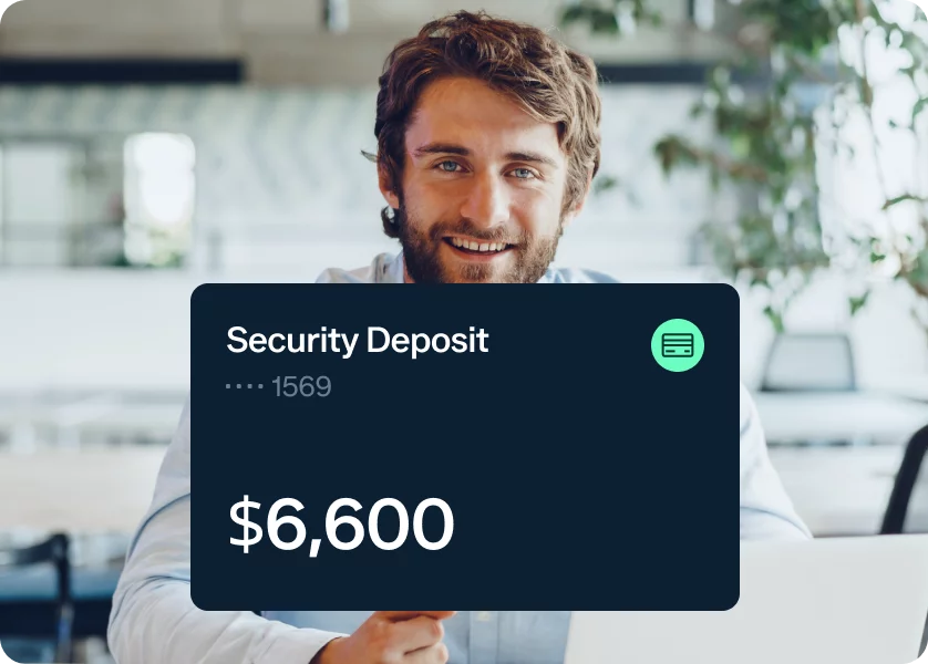 A smiling person with a beard and brown hair holds a card that says "Security Deposit" and displays a balance of $6,600. The background features a modern interior with plants and blurred furnishings.
