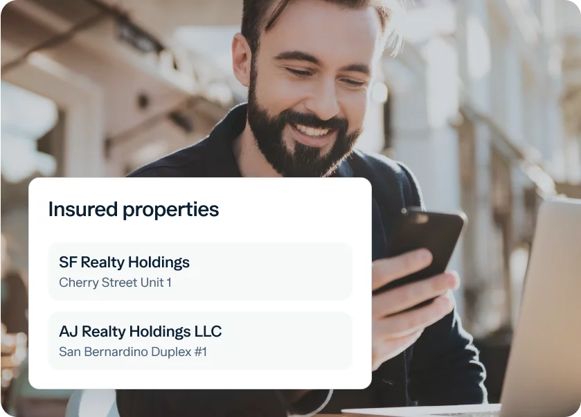 A man with a beard smiles while looking at his phone, sitting outdoors with a laptop. A white overlay on the image lists insured properties: "SF Realty Holdings, Cherry Street Unit 1" and "AJ Realty Holdings LLC, San Bernardino Duplex #1.