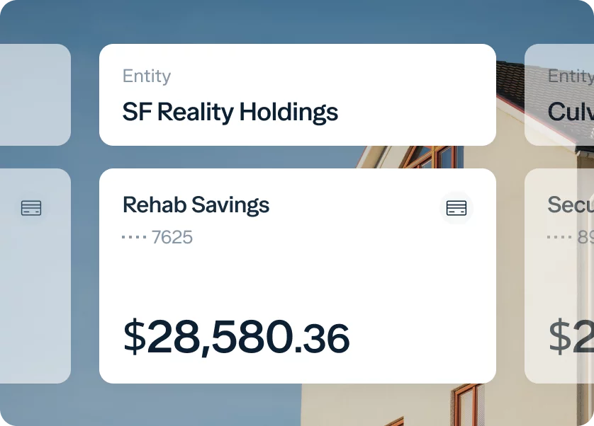 A digital dashboard displays financial information. The main card shows "Rehab Savings" with partial account number "7625" and a balance of "$28,580.36." Above it, another card is labeled "SF Reality Holdings." Part of a house and sky can be seen in the background.