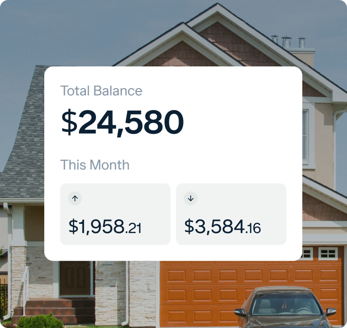 A financial dashboard displayed in front of a house shows a total balance of $24,580. Below the balance, there are two figures for the month: $1,958.21 on the left with an upward arrow and $3,584.16 on the right with a downward arrow.