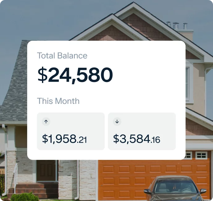 A financial dashboard displayed in front of a house shows a total balance of $24,580. Below the balance, there are two figures for the month: $1,958.21 on the left with an upward arrow and $3,584.16 on the right with a downward arrow.