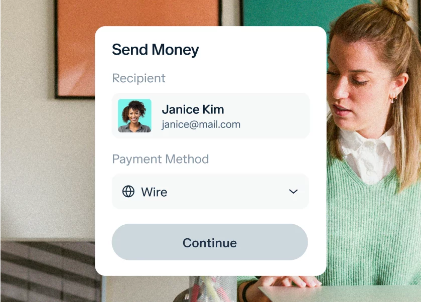 A woman in a green sweater is using a digital interface on a device. The screen shows a "Send Money" form with a recipient named Janice Kim, an email janice@mail.com, and the payment method selected as "Wire." A "Continue" button is displayed at the bottom.