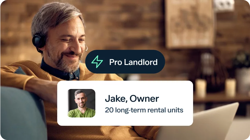 A man with gray hair and a beard, wearing an orange sweater and headset, smiles as he works on a laptop. Overlay text reads "Pro Landlord" and "Jake, Owner, 20 long-term rental units" with a small image of a man in a green shirt. The background shows a cozy, wooden room.