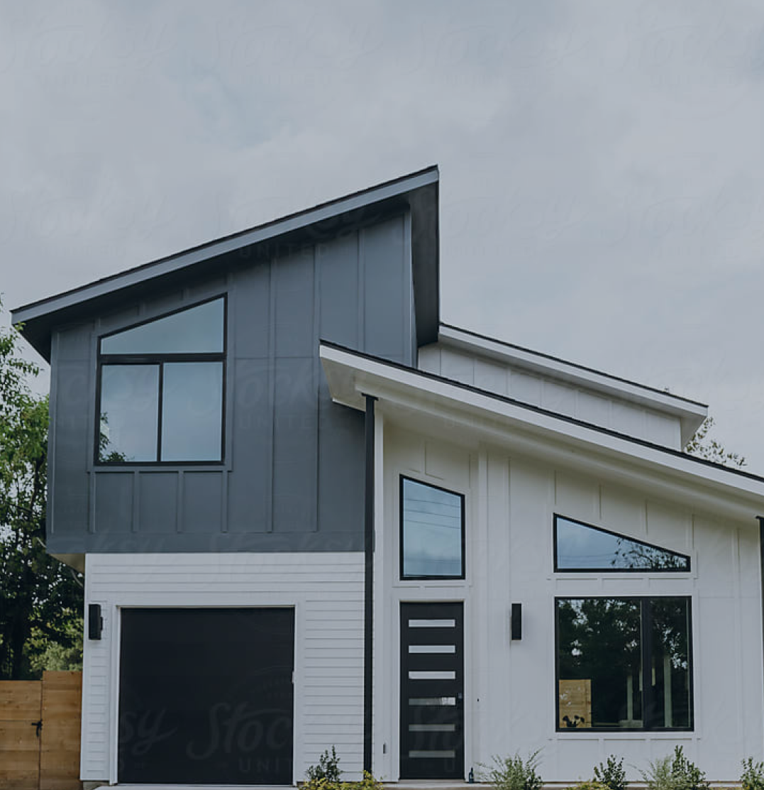 Modern two-story house with a combination of dark and light gray siding, large windows, and a sloped roof. The upper portion of the facade features vertical paneling, and the entrance has a stylish black door with multiple horizontal glass inserts.