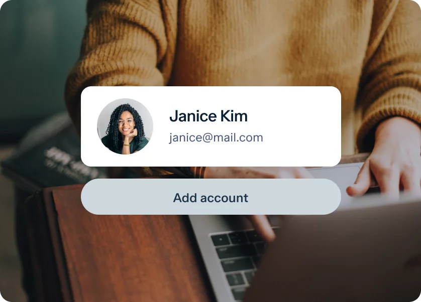 Close-up of a person typing on a laptop. In the foreground is a pop-up display showing a user profile with an image, the name "Janice Kim," an email address "janice@mail.com," and a button labeled "Add account." The person is wearing a mustard-colored sweater.