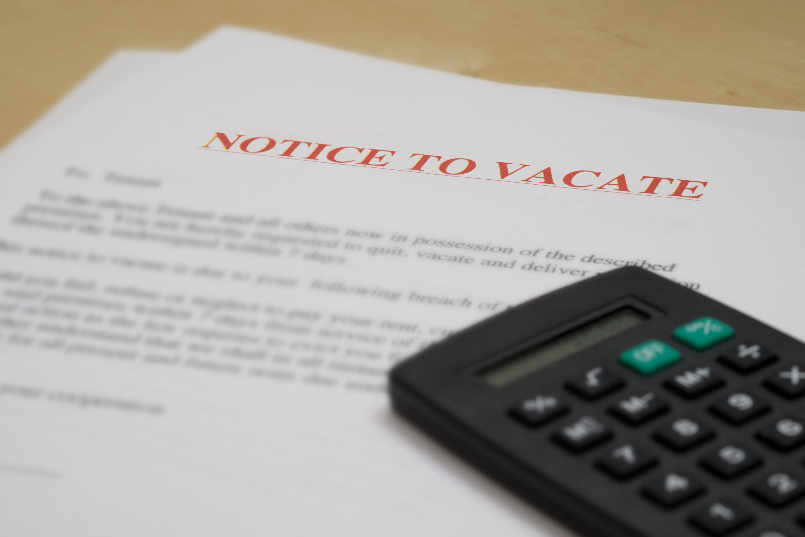 A "Notice to Vacate" document is partially visible on a table. The notice text is bold in red at the top. A black calculator rests beside the paper. The background is a neutral surface.