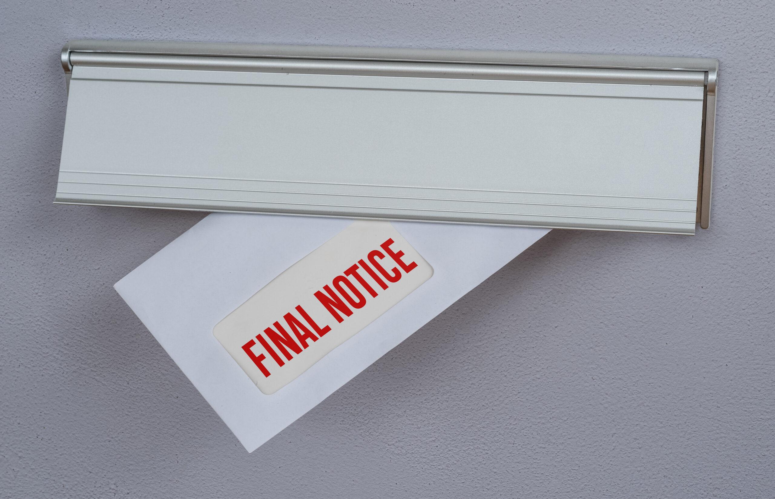 A white envelope with a red "FINAL NOTICE" label is partially inserted through a silver mail slot on a gray surface.