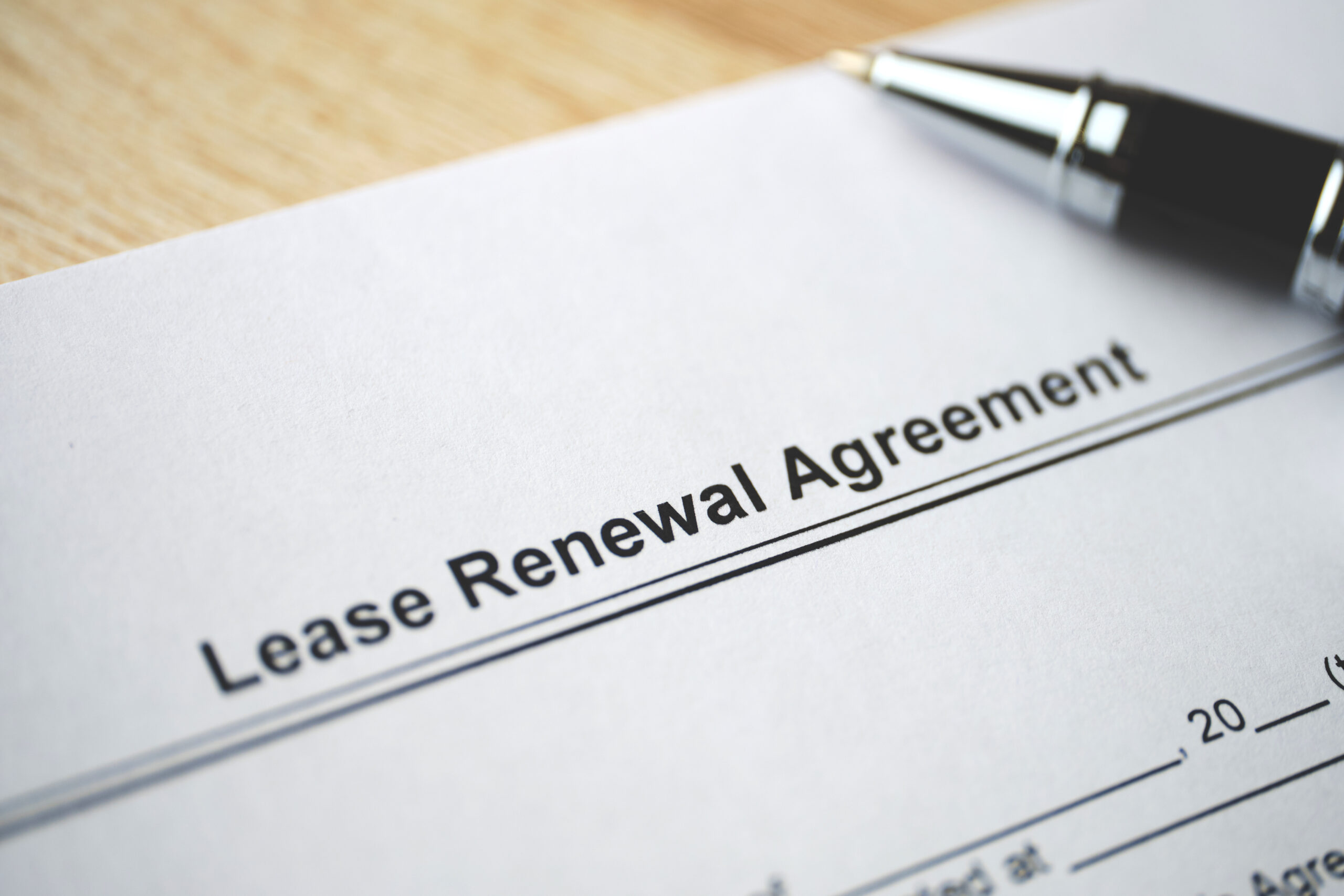 Close-up of a lease renewal agreement document with a pen resting on top, suggesting a signature is needed.