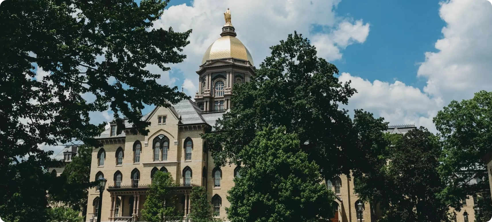 A historic building with a large golden dome surrounded by green trees under a partly cloudy sky.