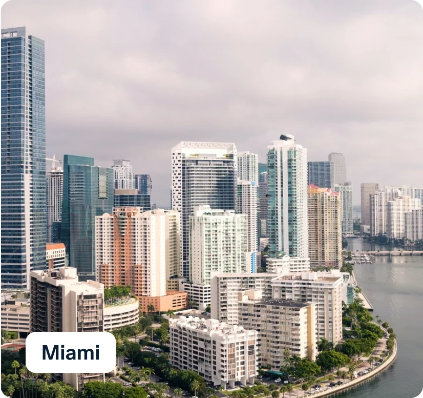 Aerial view of downtown Miami, showcasing a skyline of modern high-rise buildings along the waterfront under a cloudy sky.