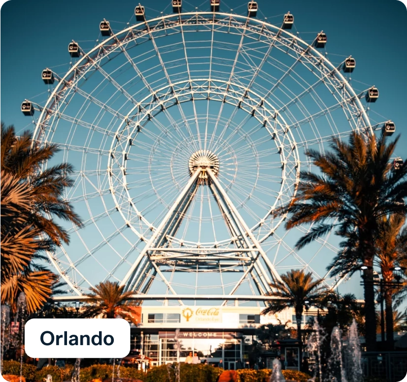 A large Ferris wheel dominates the scene, set against a clear blue sky. Palm trees frame the foreground, and a sign reads "Orlando" in the bottom left corner.