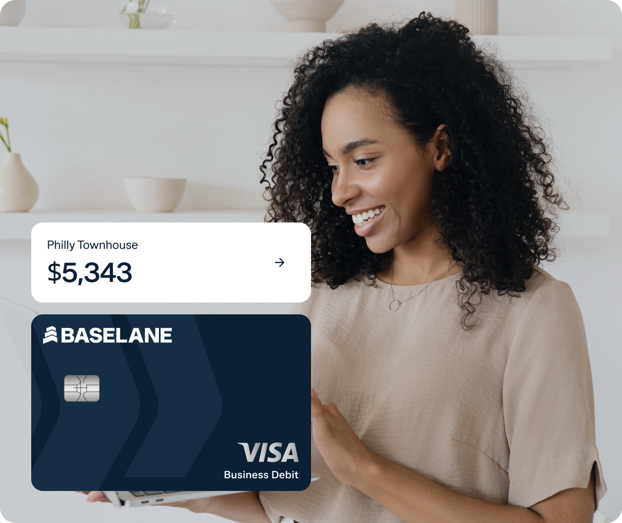 A person with curly hair is smiling while looking at a tablet. The image features a digital graphic of a Visa business debit card with Baseline branding and a label that reads "Philly Townhouse $5,343.