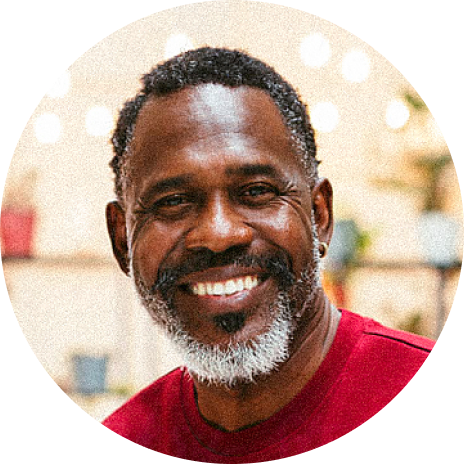 Smiling man with a gray beard, wearing a red shirt, against a softly blurred background.