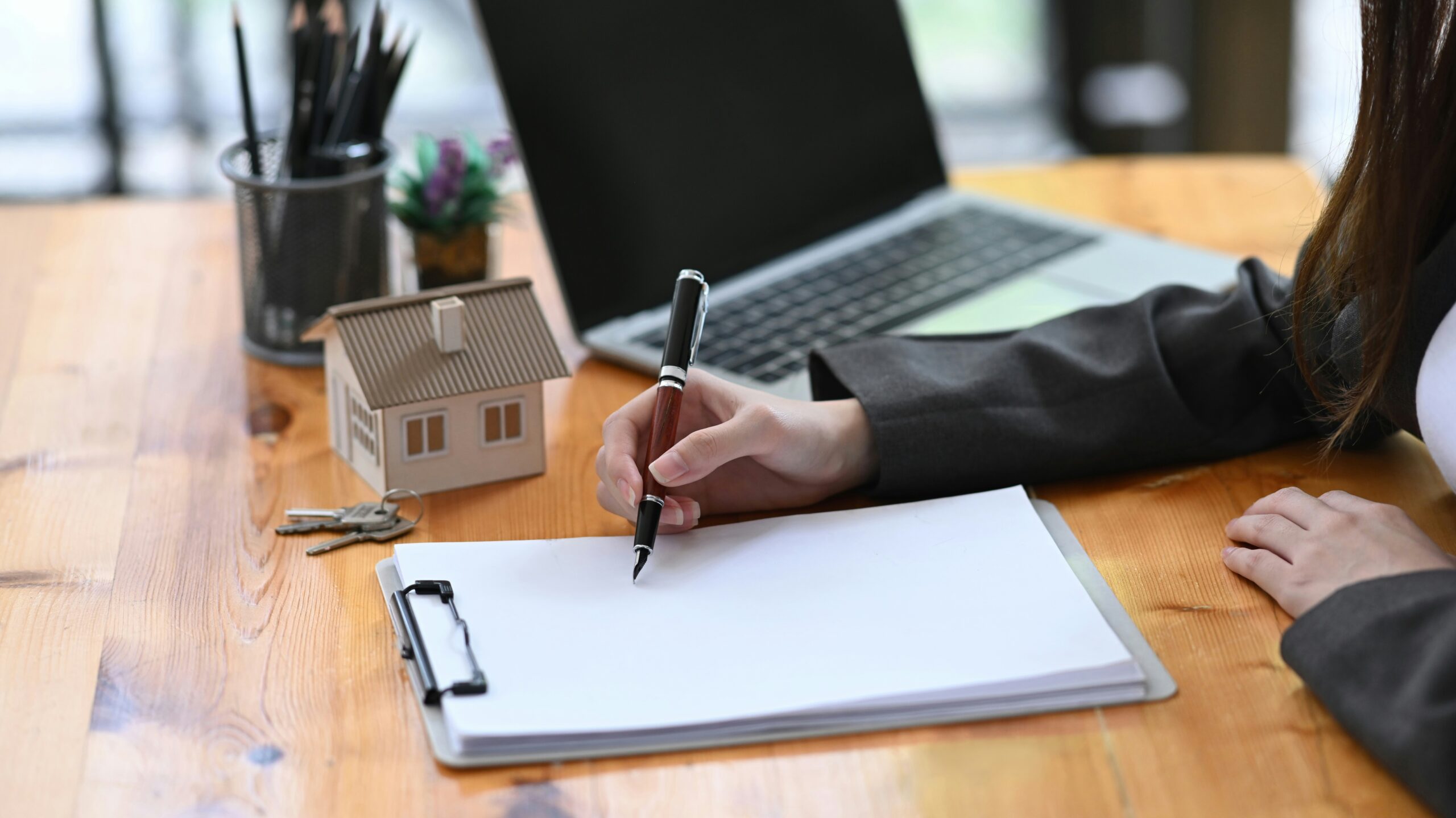 Investment property mortgage rates concept with investor signing documents, model house, keys, and laptop on a desk.
