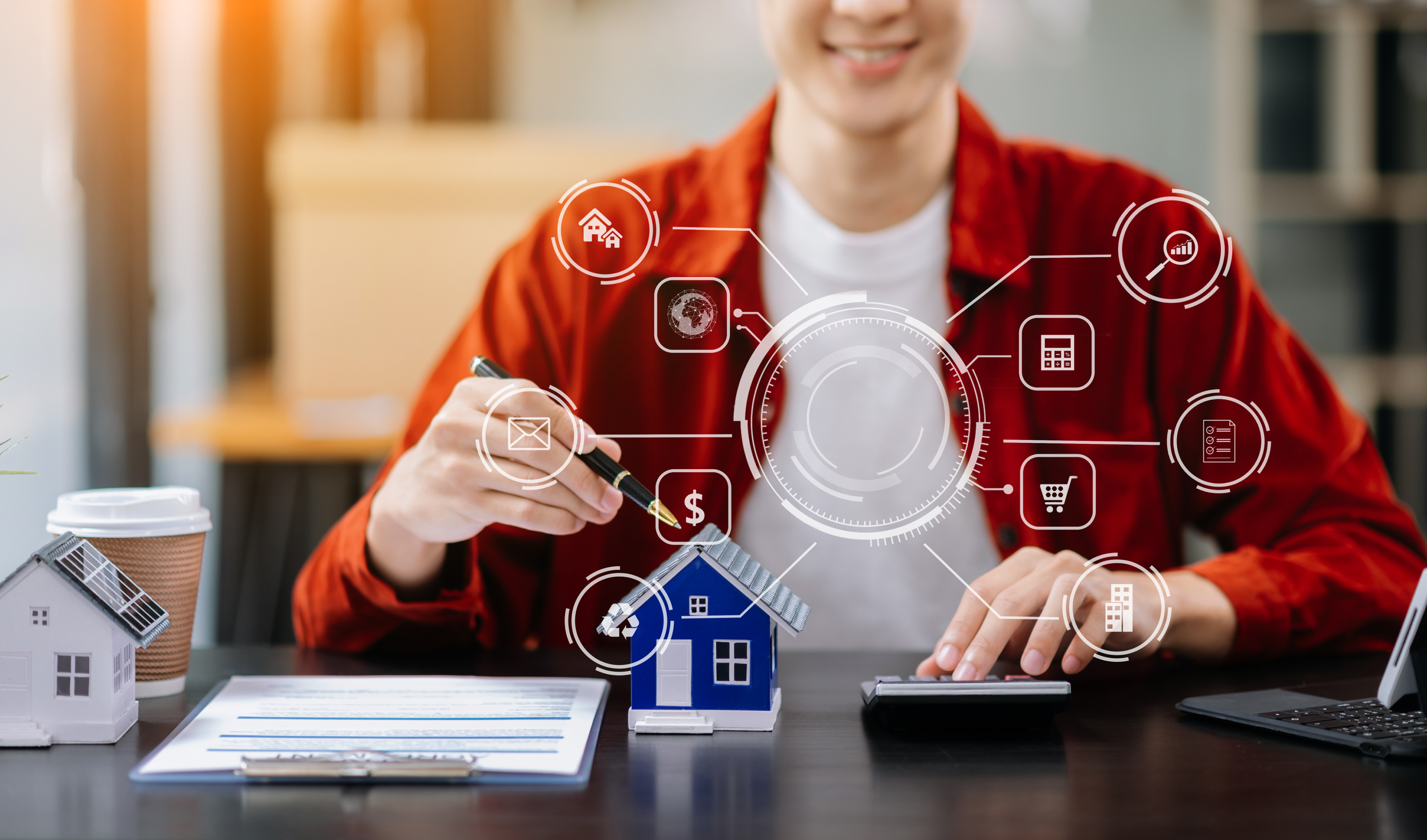 A person in a red shirt calculates finances at a desk with a miniature house model, clipboard, and coffee cup, while virtual icons highlight business vs personal bank account​ topics related to real estate and finance.