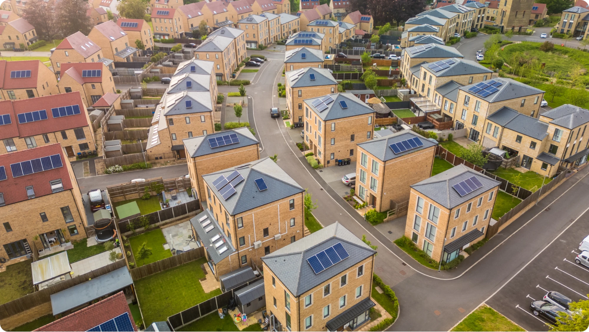 Aerial view of a modern suburban neighborhood with rows of brick houses, many featuring solar panels on their roofs—much like learning how to structure business bank accounts for efficient management—surrounded by green lawns and fenced gardens along curved streets.