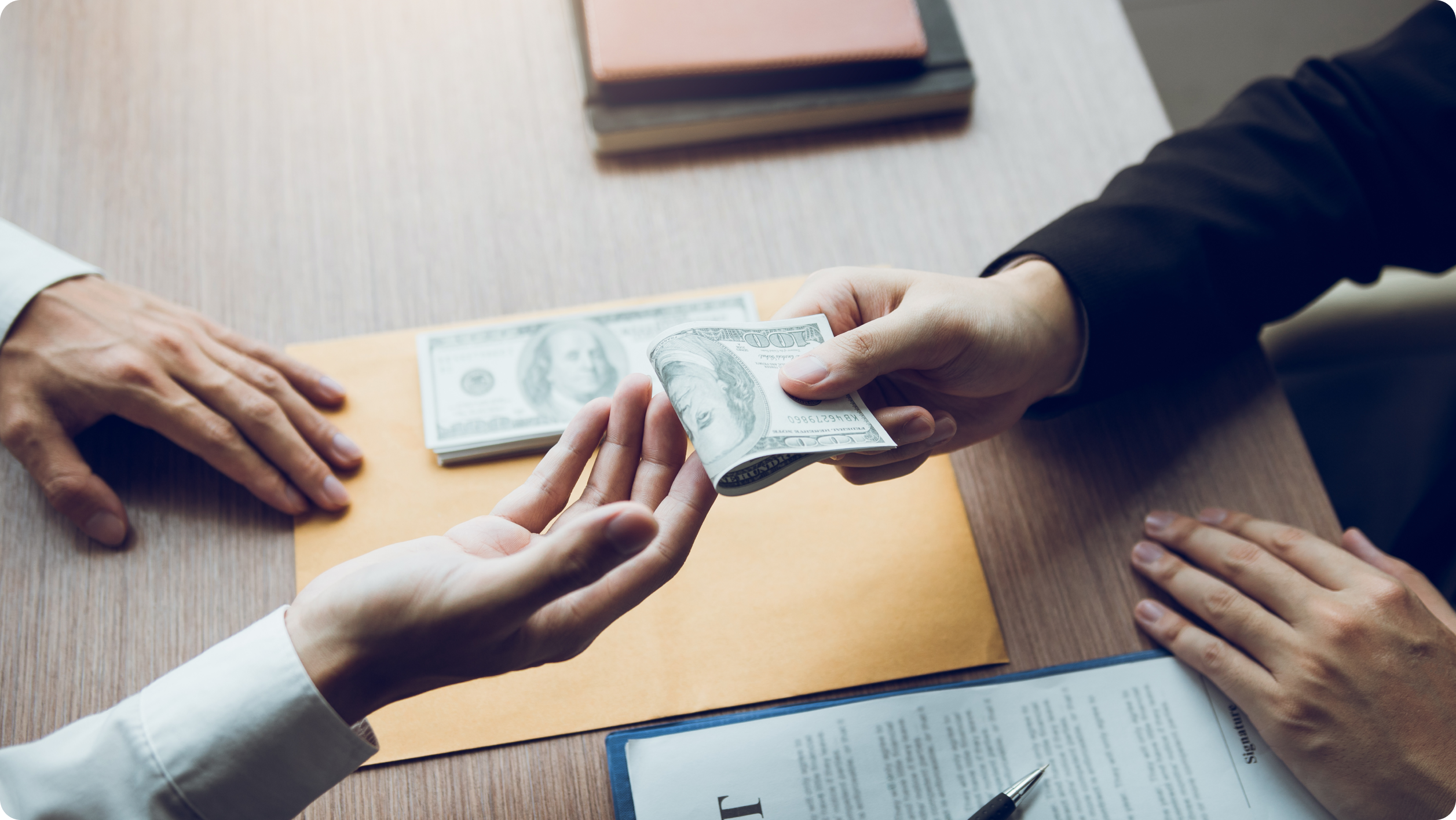 Two people exchange a stack of U.S. hundred dollar bills over a desk, with documents and an envelope visible, suggesting a financial transaction or discussion related to HOA bank services.