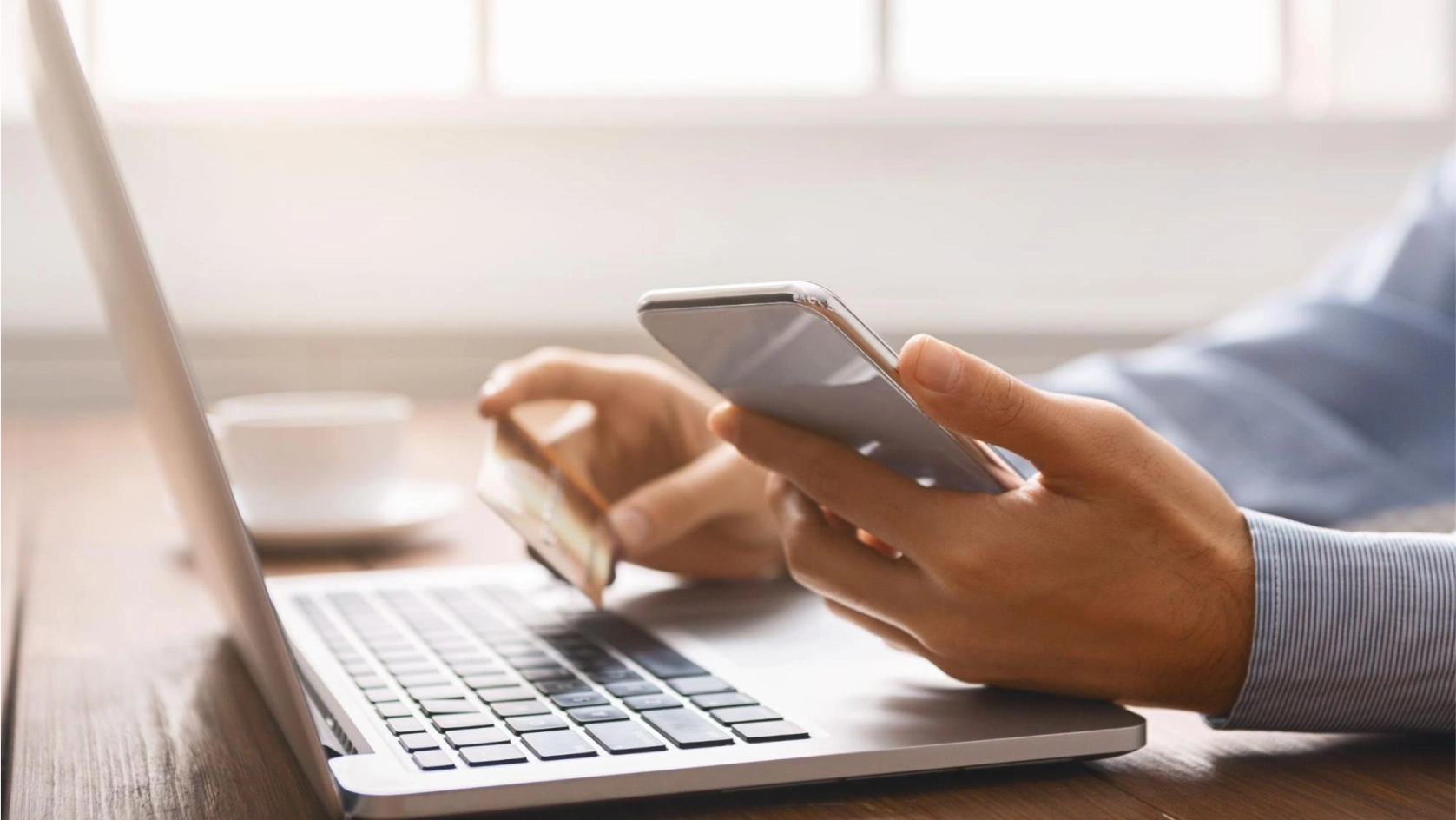 A person holding a smartphone and a credit card, sitting at a desk with an open laptop, appears to be making an online payment—possibly managing an AI bank account for real estate transactions.