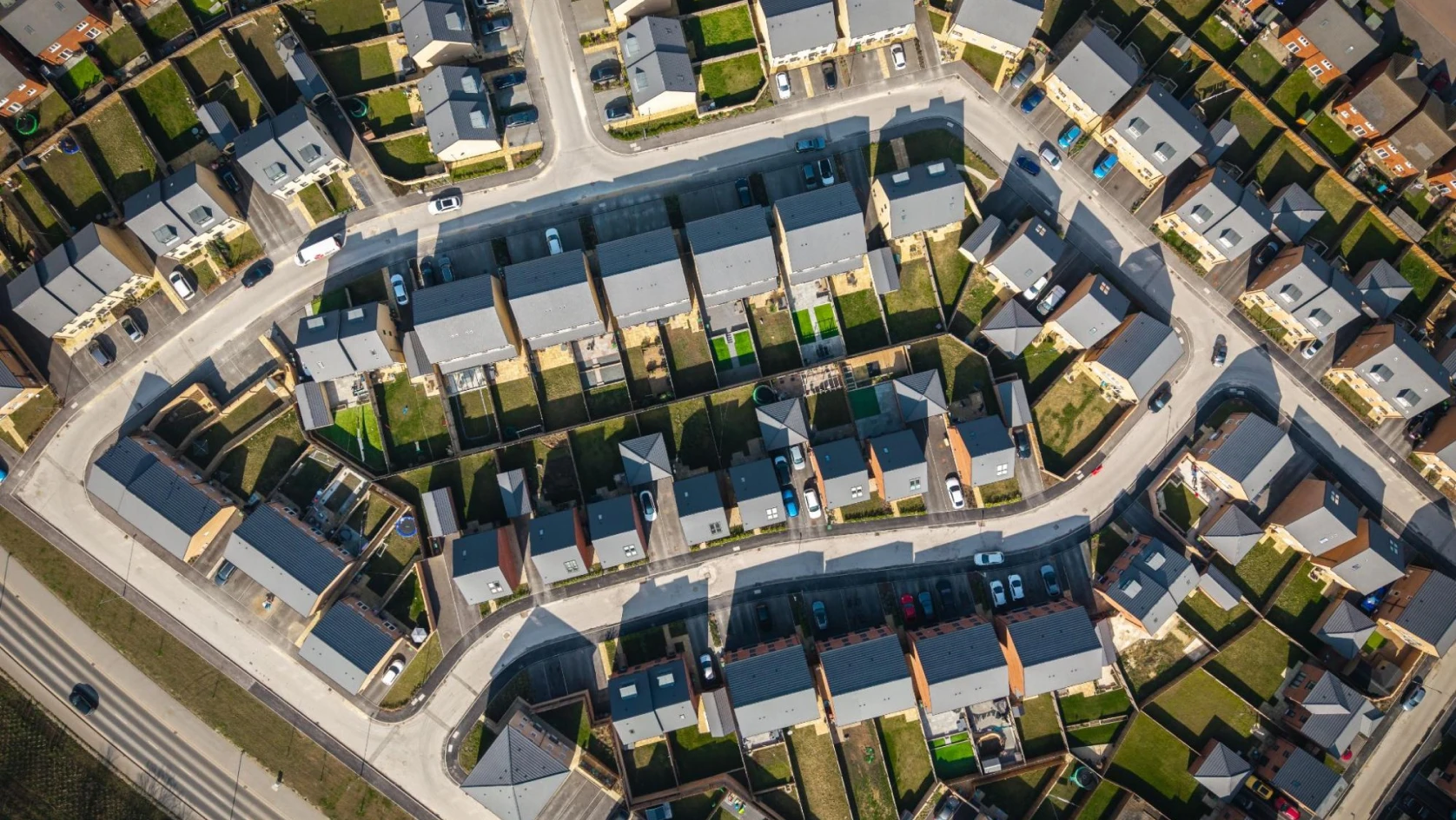 Aerial view of a suburban neighborhood with rows of houses, green lawns, and cars parked along curved residential streets—an organized setting ideal for managing properties with an AI bank account for real estate investments.