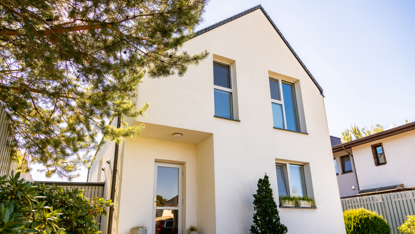 Modern two-story white house with large windows, a sloped roof, and minimal landscaping—including shrubs and a tree in the foreground—under a clear blue sky, as streamlined as the best AI accounting software.